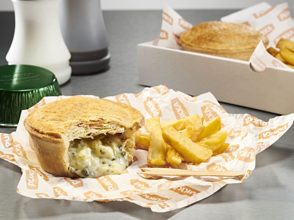 A Pukka pie broken open to show its filling, beside a portion of chips and a wooden chip fork on branded paper